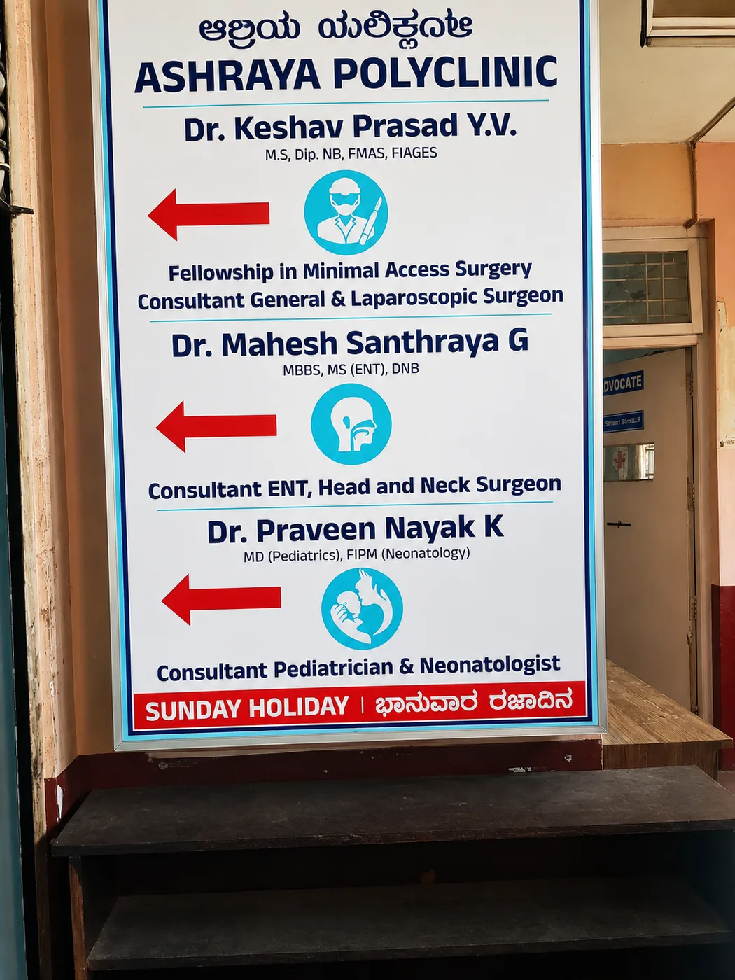 Ashraya Polyclinic entrance board listing Dr. Mahesh Santhraya G